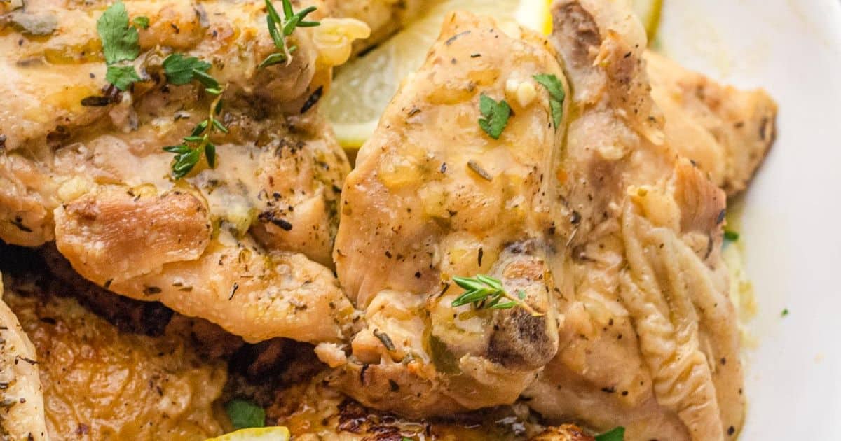 Close-up of seasoned baked chicken breasts garnished with fresh herbs and lemon slices.