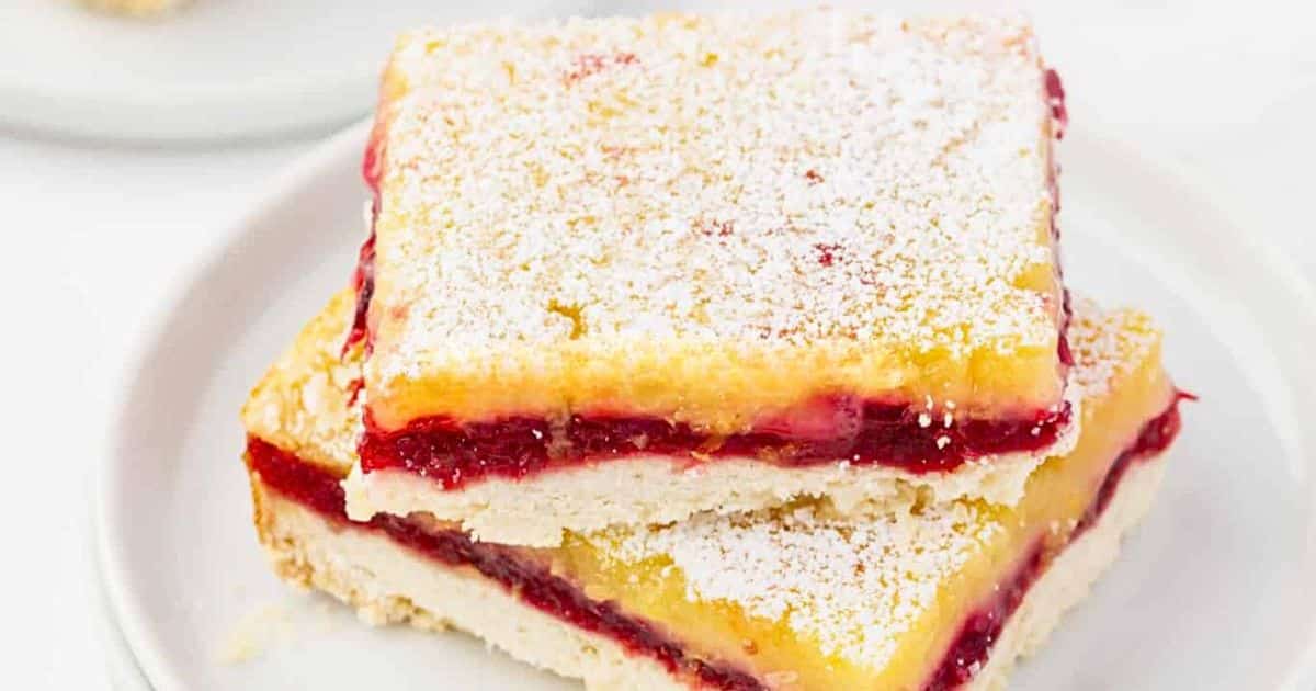 Two layered dessert bars with a red fruit filling and powdered sugar on top, stacked on a white plate.