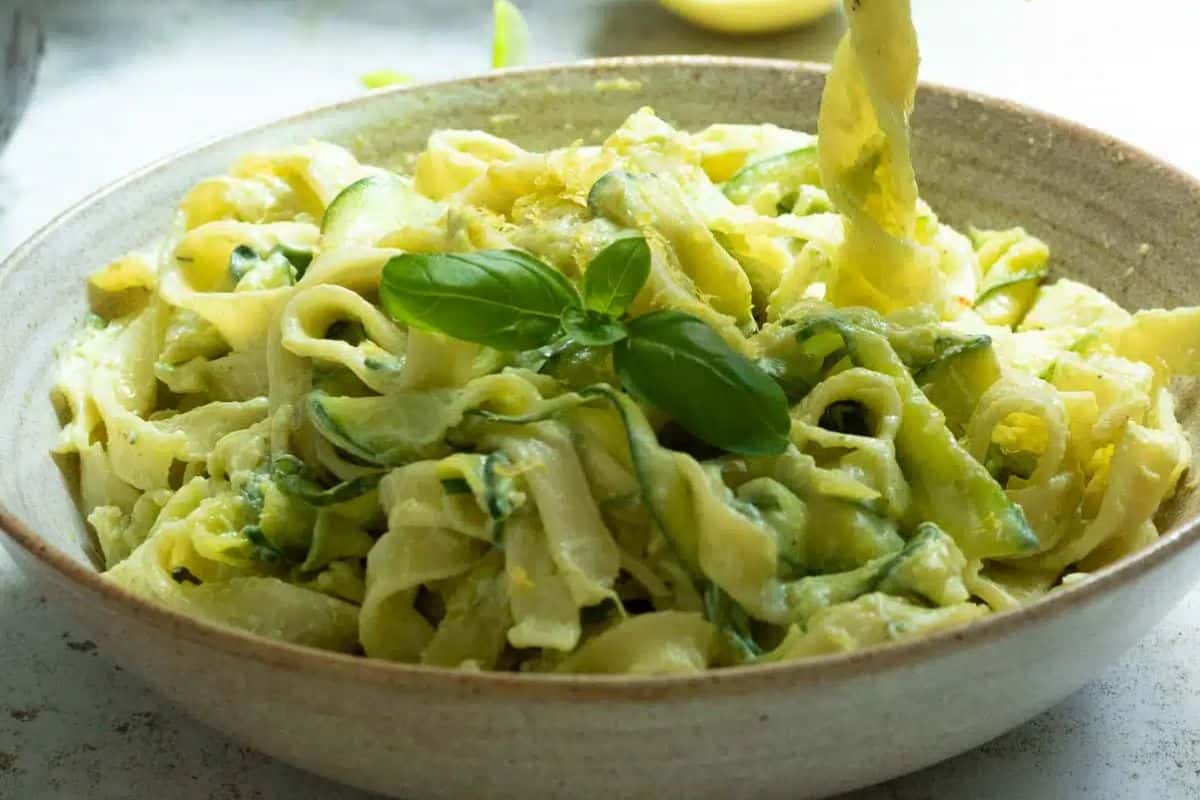 A bowl of creamy zucchini pasta garnished with fresh basil leaves.