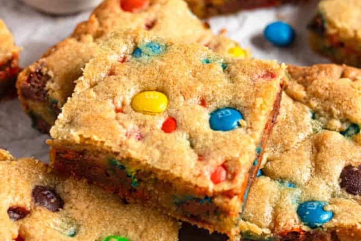 Close-up of M&M cookie bars stacked on top of each other, showing colorful candies and chocolate chips.
