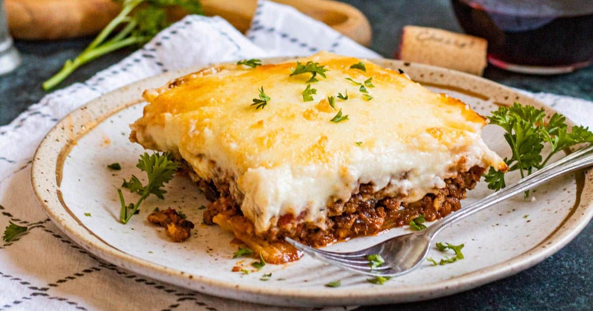 A slice of cheesy baked lasagna garnished with parsley on a plate with a fork.