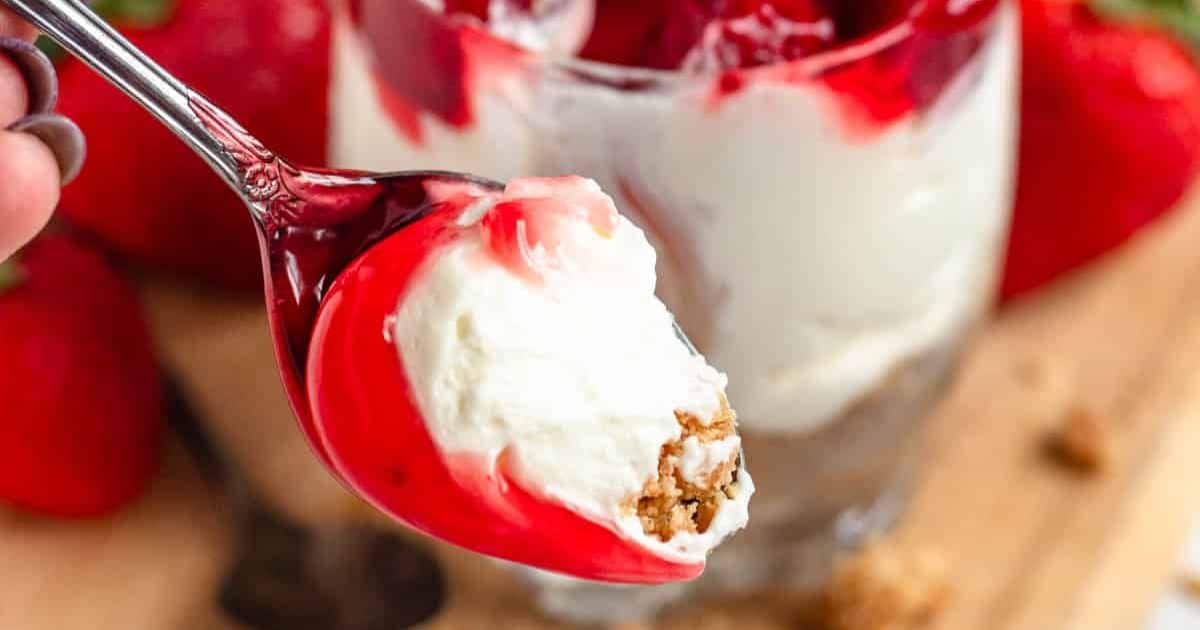 A spoonful of creamy cheesecake dessert with strawberry sauce and graham cracker crust.