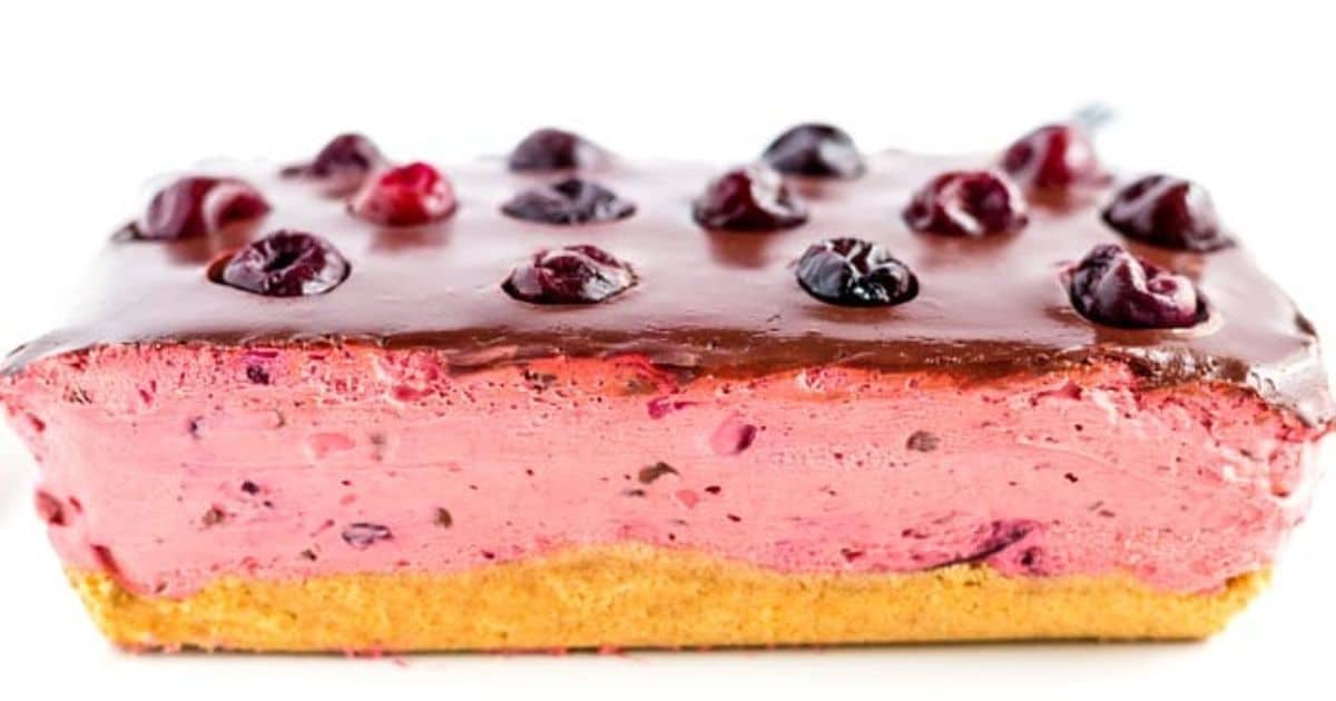 Rectangular cherry mousse cake with chocolate glaze, topped with cherries, and a yellow biscuit base.