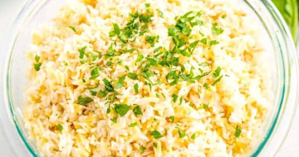 A glass bowl filled with cooked rice, garnished with chopped fresh herbs on top.