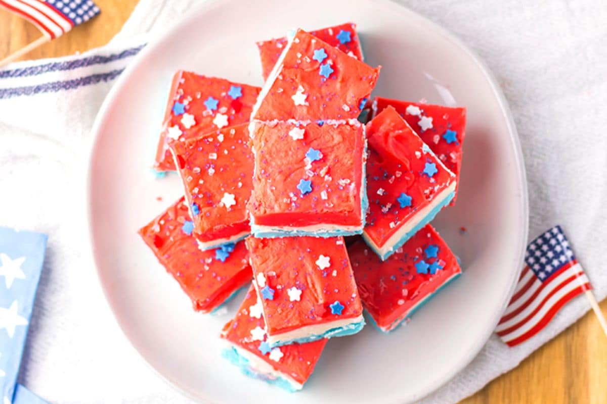 Red, white, and blue fudge squares with star sprinkles on a plate, next to small American flags.