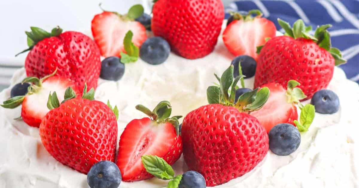 Whipped cream cake topped with whole strawberries, blueberries, and mint leaves.