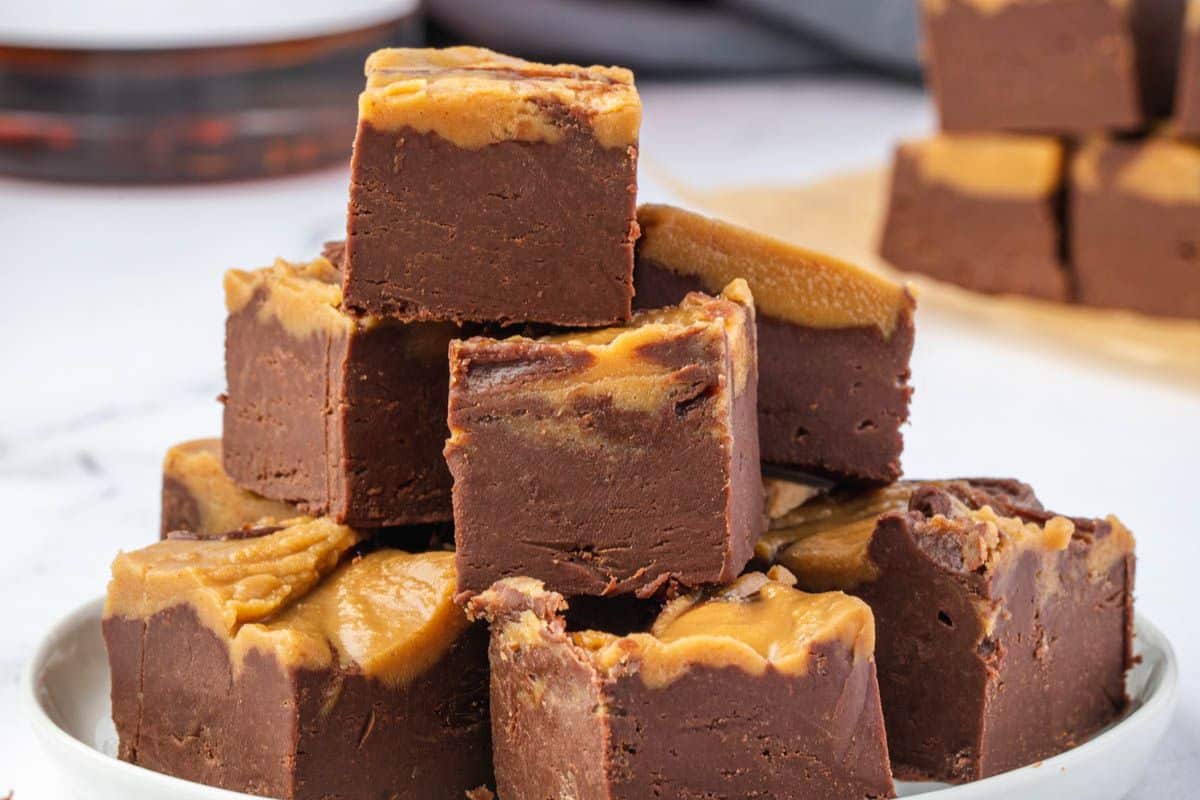 A plate stacked with pieces of chocolate and peanut butter fudge, with a creamy peanut butter swirl on top.