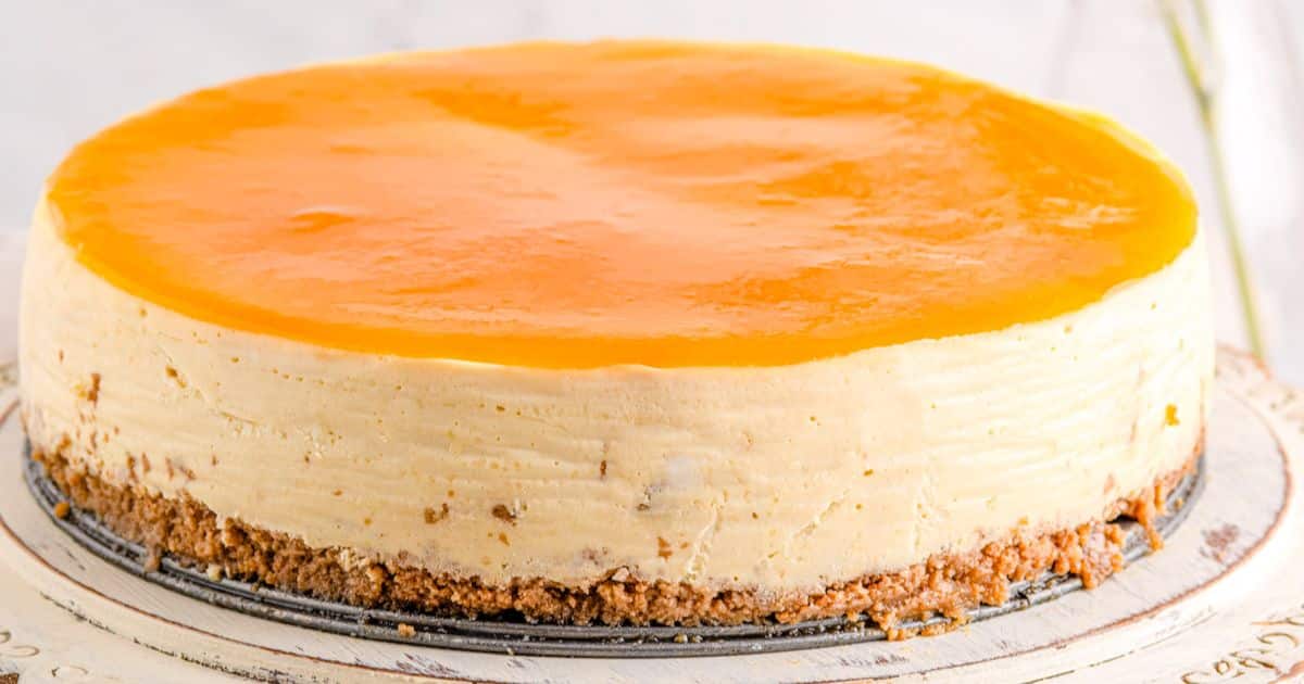 A round cheesecake with a smooth, glossy orange glaze on top and a crumbly crust at the bottom.