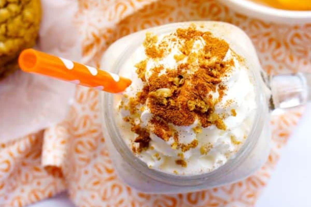 A creamy milkshake topped with whipped cream, cinnamon, and cookie crumbs, served with an orange straw.