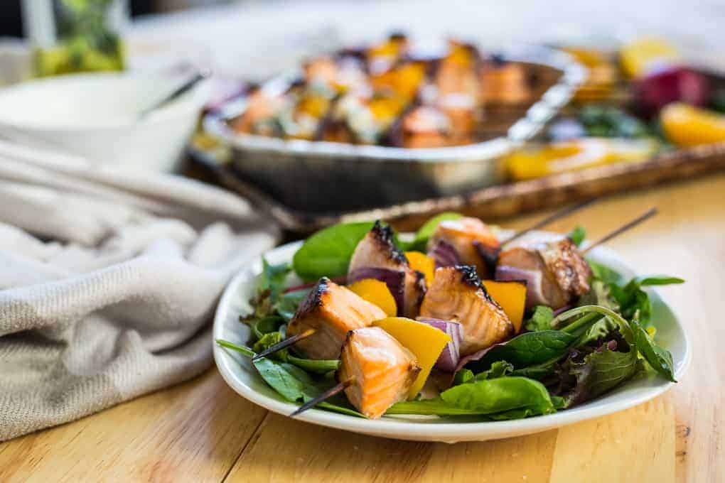 Grilled salmon and veggie skewers served on a bed of mixed greens on a white plate.
