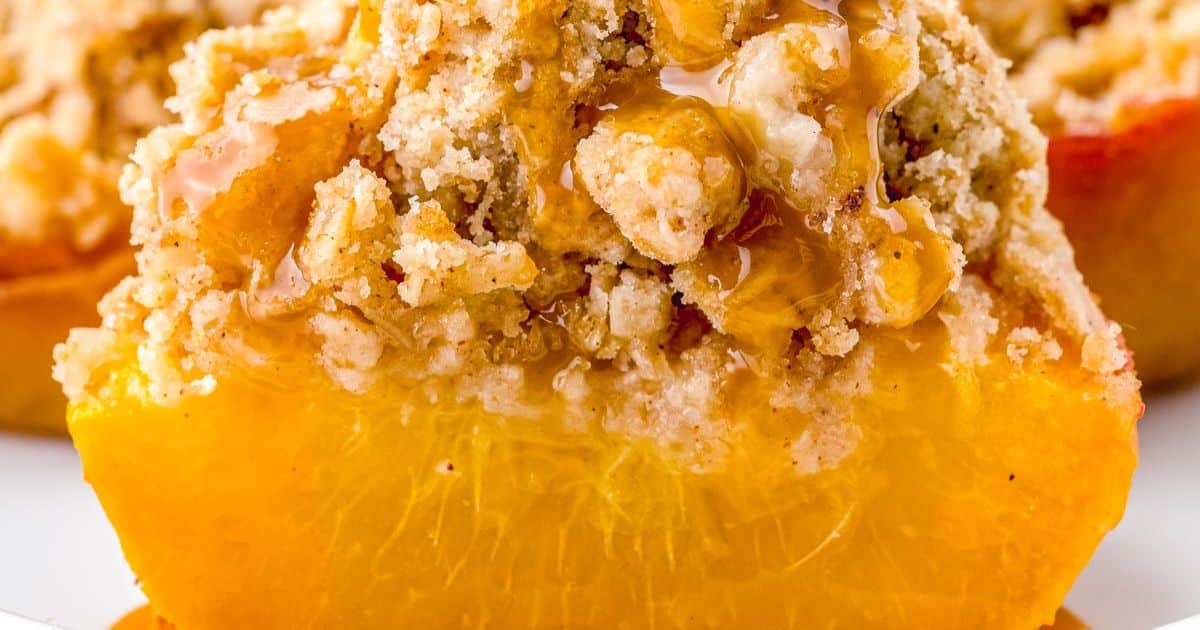 A close-up of a baked peach half topped with crumbly streusel and drizzled with honey.