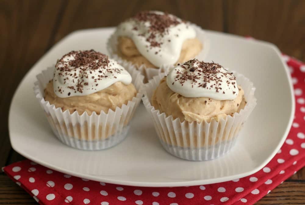 Three cupcakes with cream and chocolate shavings on top, served on a white plate with a red polka dot napkin.