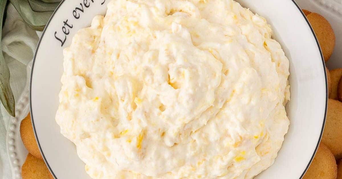 A bowl of fluffy, creamy dip surrounded by round vanilla cookies on a white plate.