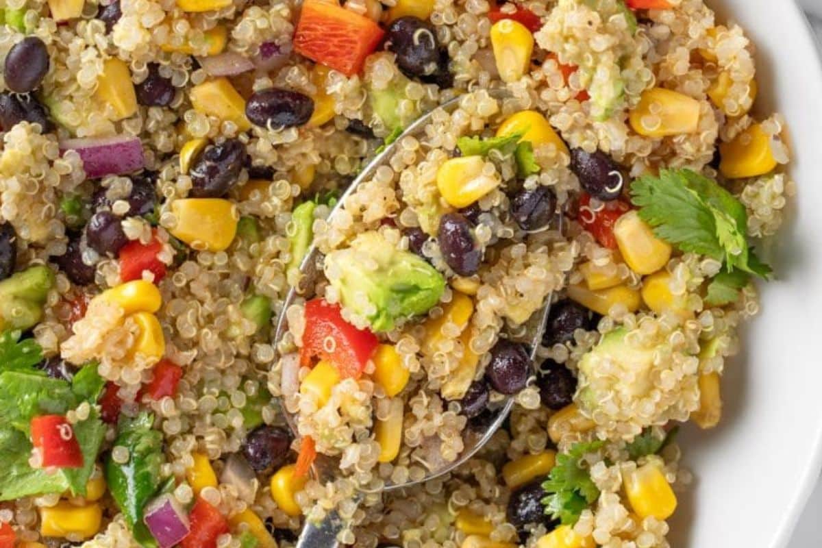 Quinoa salad with black beans, corn, avocado, red pepper, red onion, and cilantro on a white plate.
