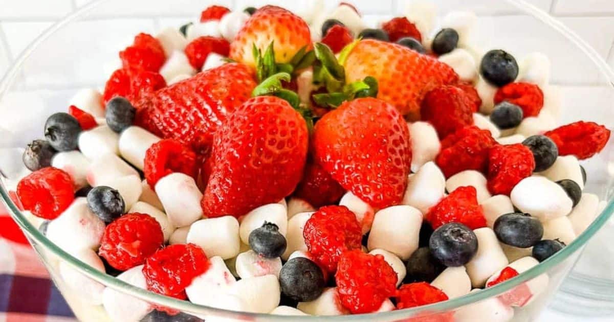A glass bowl filled with strawberries, raspberries, blueberries, and mini marshmallows.