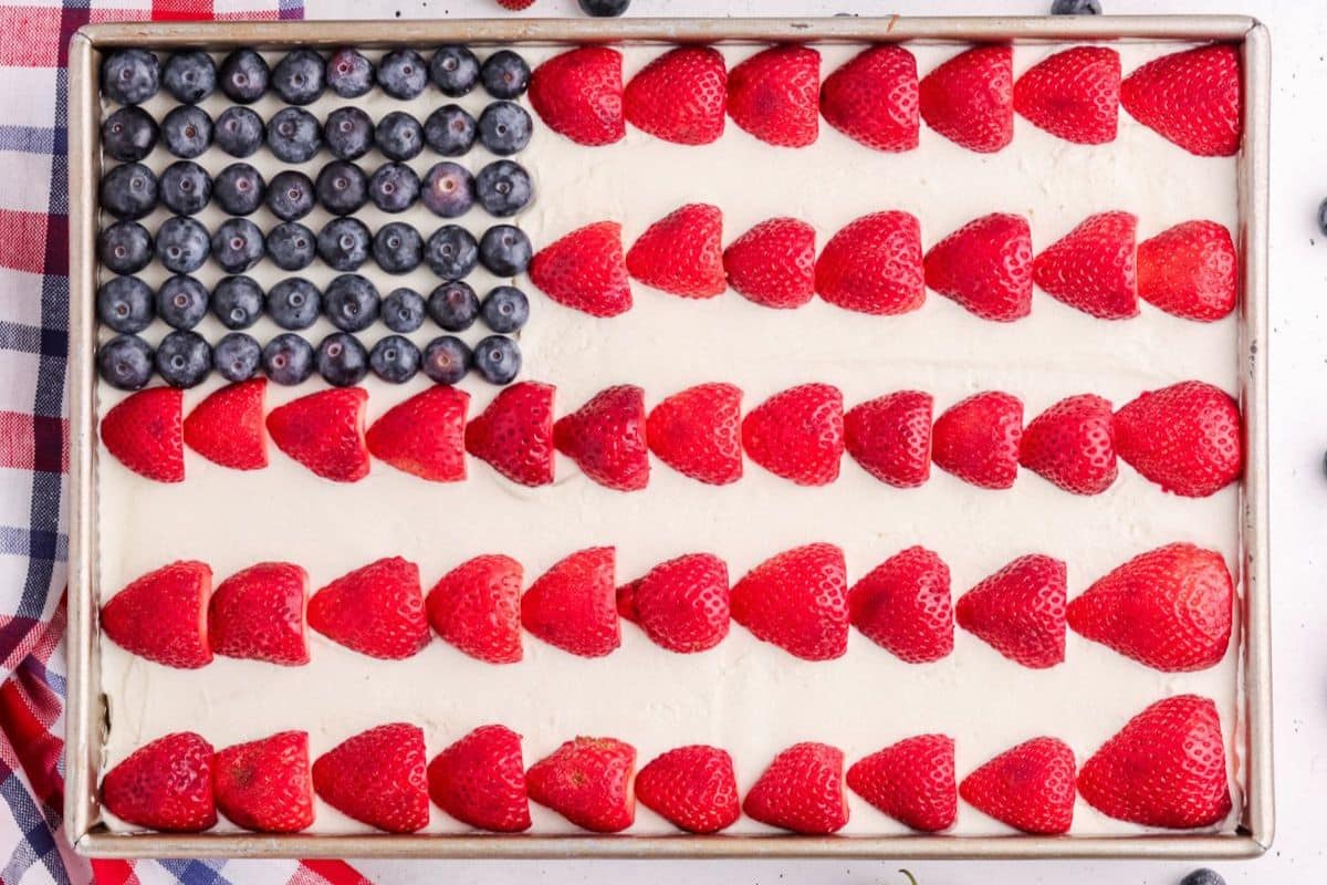 A sheet cake decorated like an American flag with blueberries and rows of sliced strawberries on white frosting.
