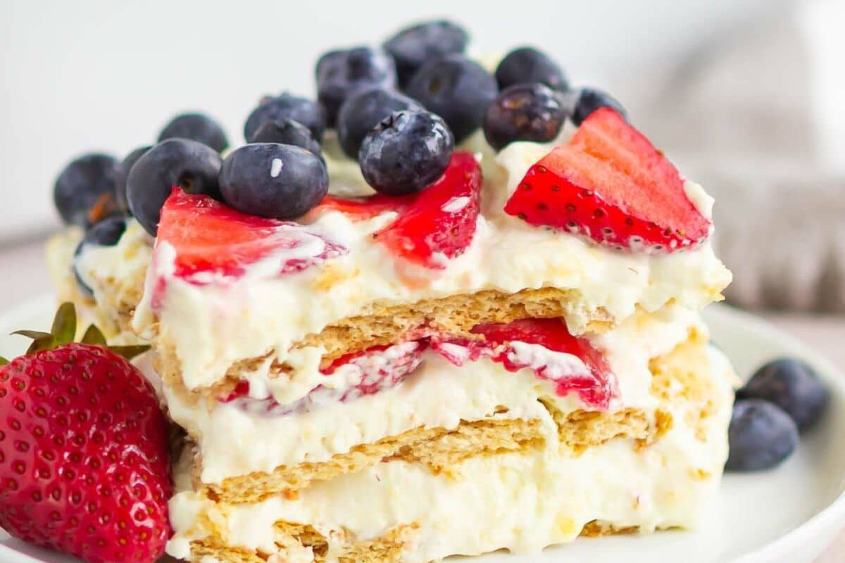 A layered dessert with cream, graham crackers, strawberries, and blueberries on a plate.