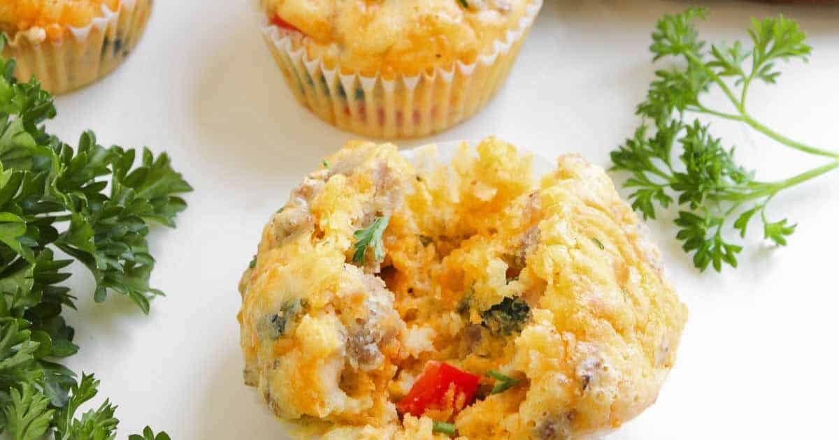 A savory muffin with herbs and vegetables, broken open on a white surface, surrounded by parsley sprigs.