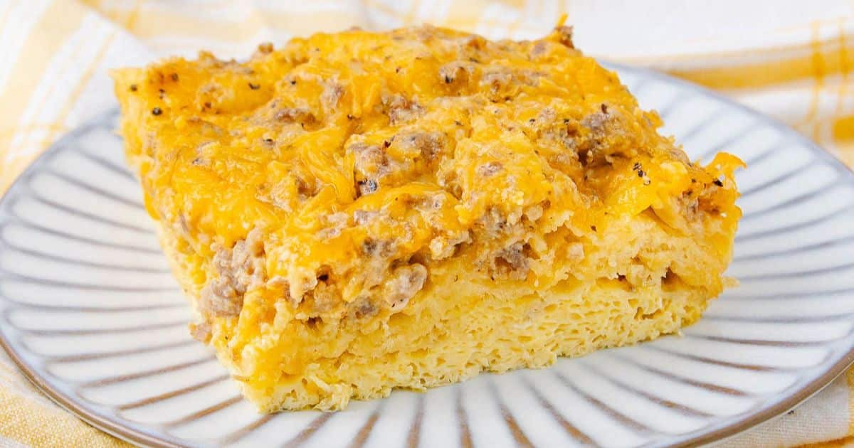 A slice of cheesy breakfast casserole with sausage on a white plate with gray stripes.