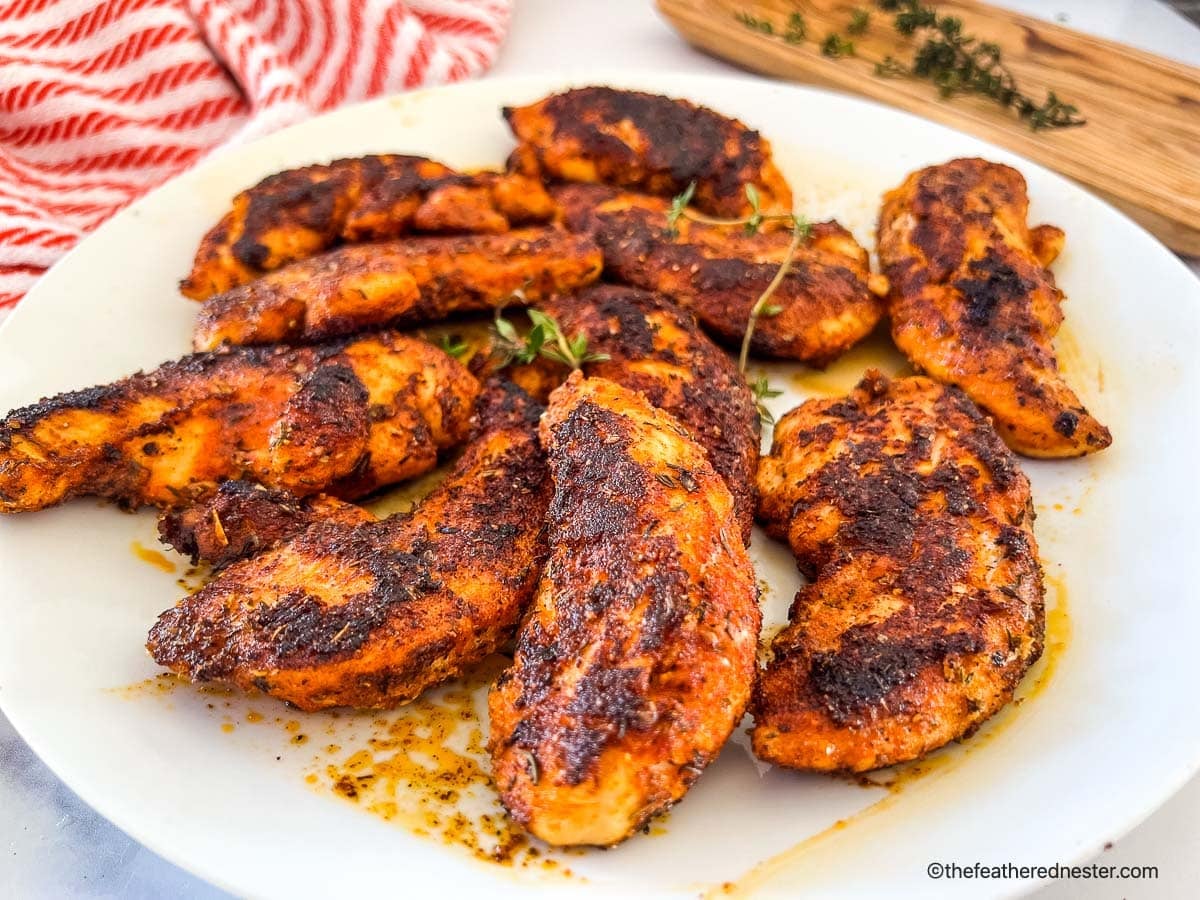A plate of seasoned, cooked chicken tenders garnished with fresh herbs on a white plate.