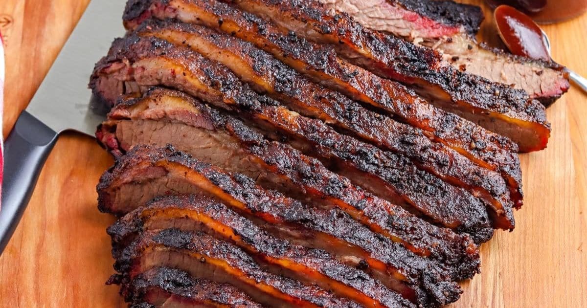 Sliced smoked brisket with a dark, crispy bark arranged on a wooden cutting board.