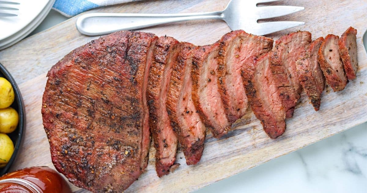 Sliced, cooked roast beef on a wooden cutting board with a serving fork nearby.