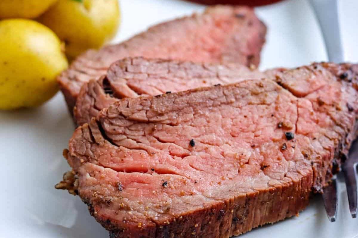 Three slices of medium-rare roast beef on a plate with small yellow potatoes in the background.