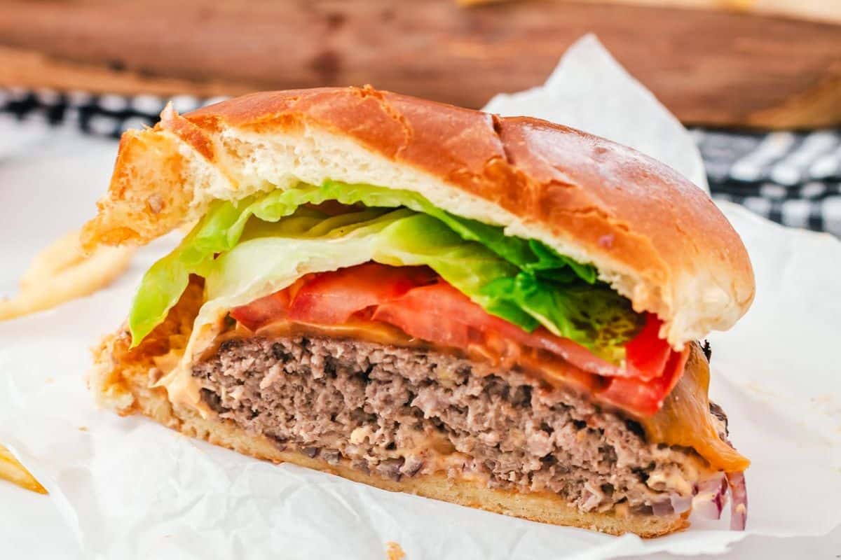 Half-eaten cheeseburger with lettuce, tomato, and onion on a white wrapper.