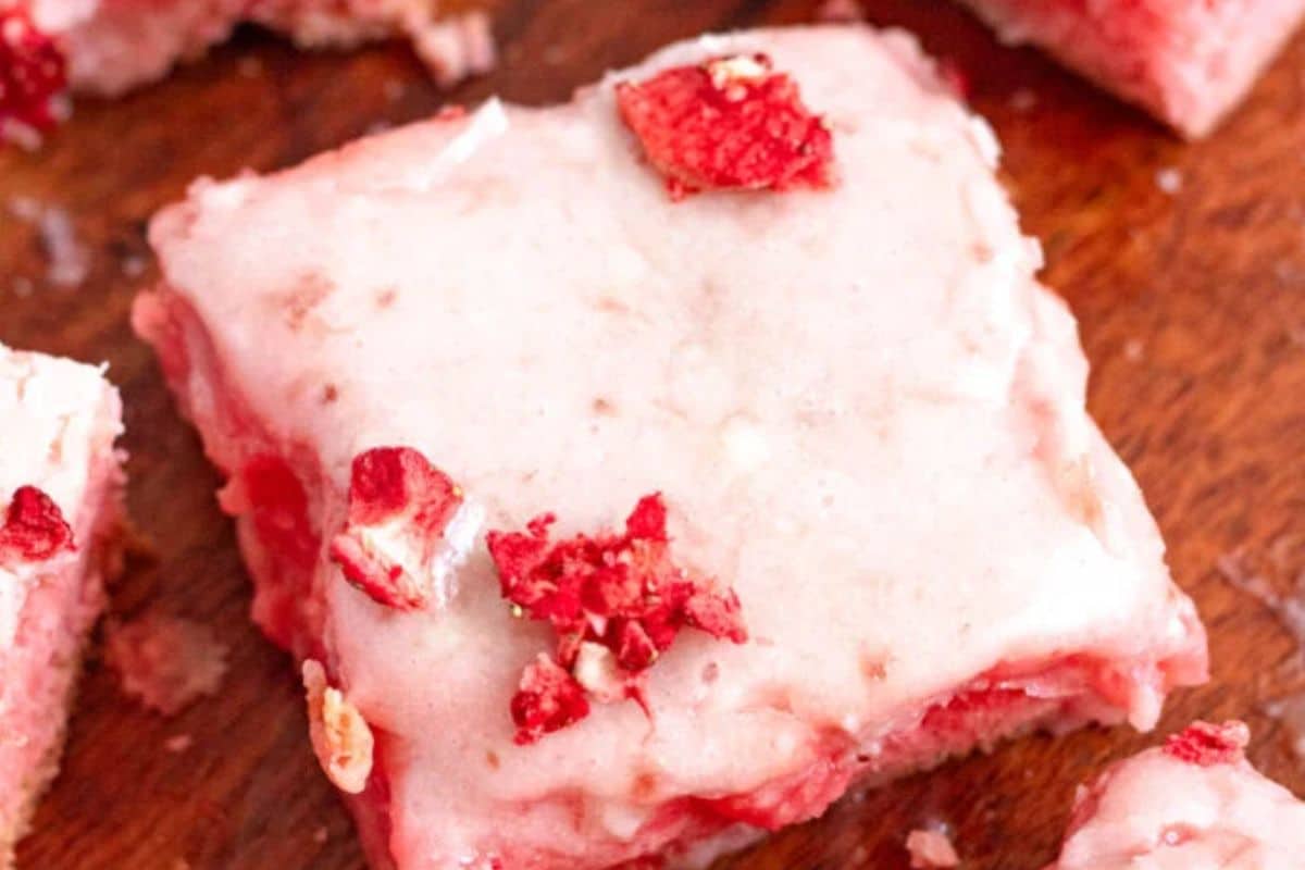 A frosted strawberry dessert bar topped with bits of dried strawberries on a wooden surface.