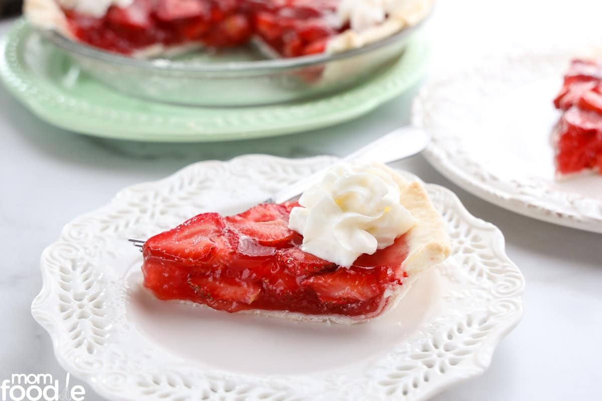 A slice of strawberry pie topped with whipped cream on a decorative white plate.
