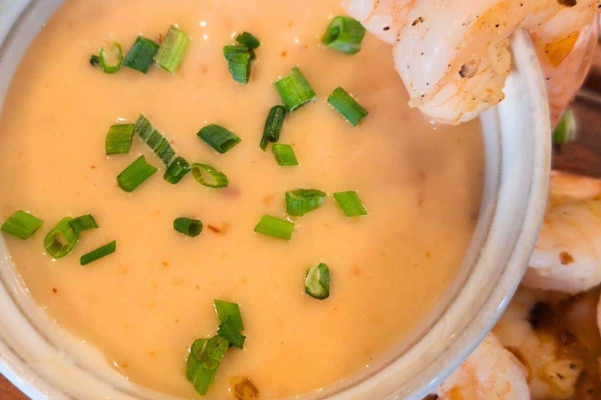 Creamy dipping sauce topped with chopped green onions, with shrimp on the side of the bowl.