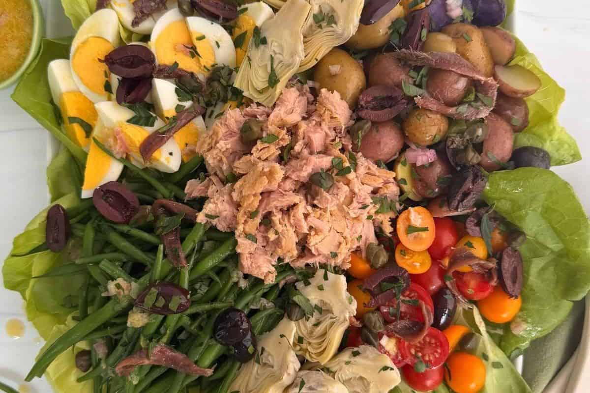 A salad platter with tuna, boiled eggs, potatoes, green beans, artichokes, olives, and cherry tomatoes.