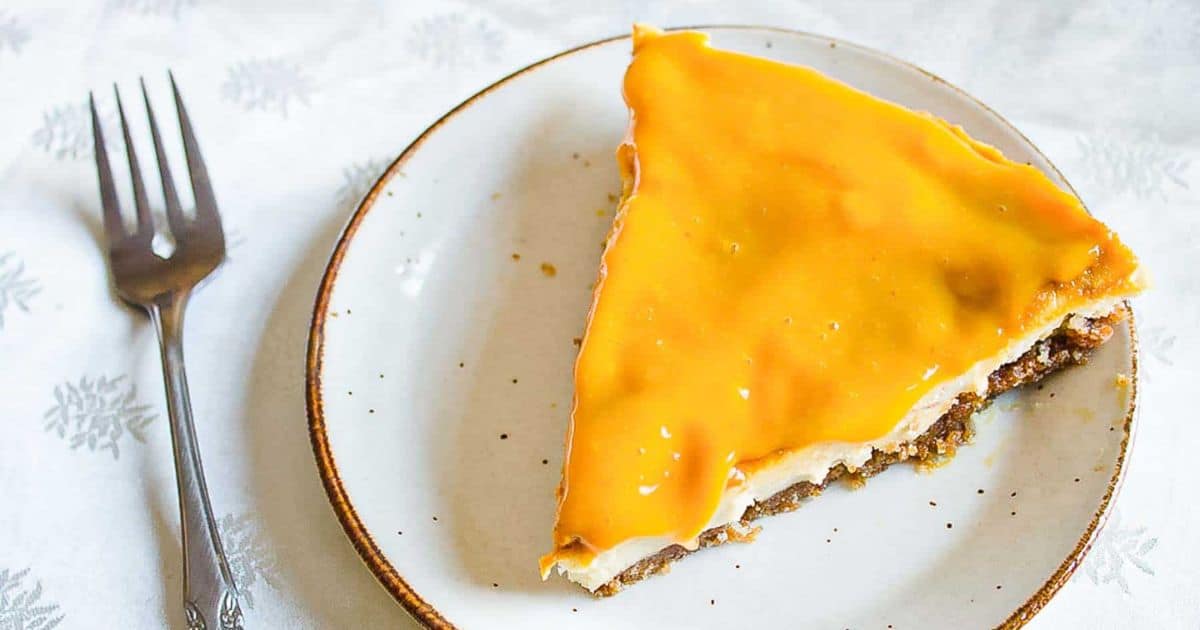 A slice of pie with a shiny orange glaze on a plate, next to a fork on a white tablecloth.