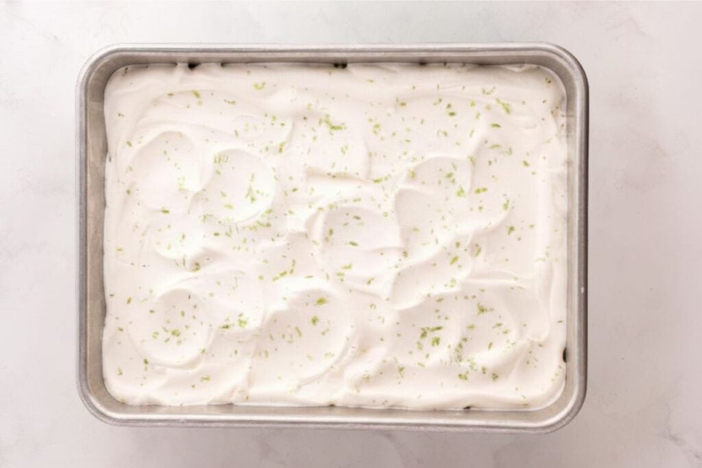 Rectangular pan filled with creamy, white dessert topped with grated lime zest on a light surface.