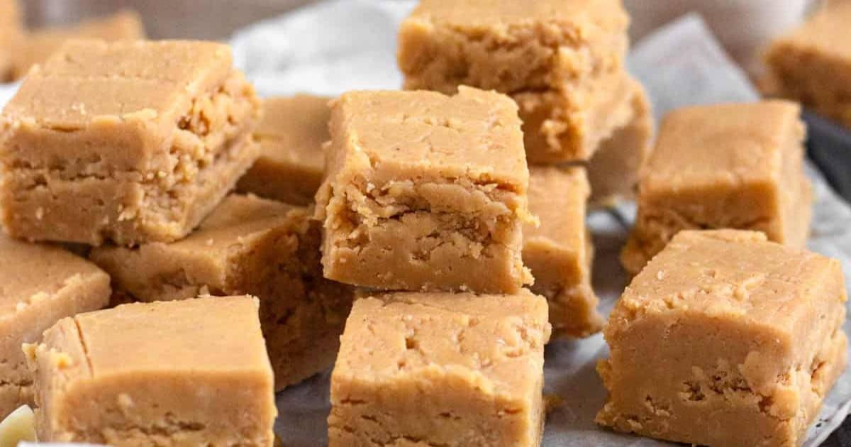 Squares of creamy peanut butter fudge stacked on parchment paper.
