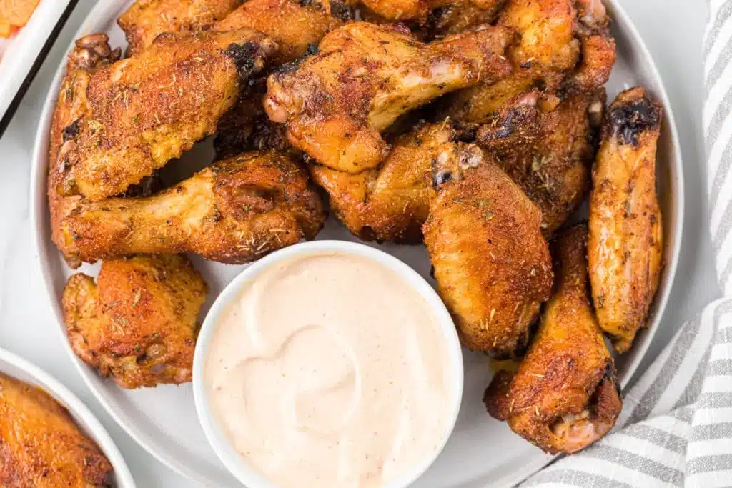 A plate of seasoned chicken wings with a bowl of creamy dipping sauce on the side.