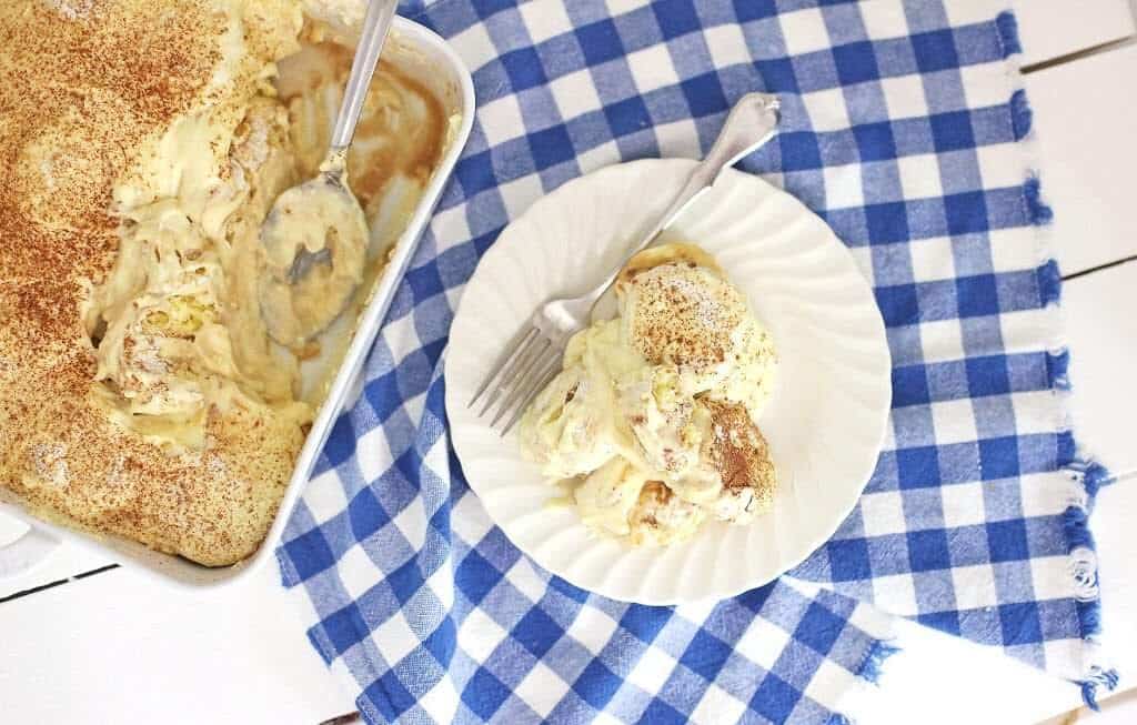 A plate with creamy dessert and a fork, next to a baking dish on a blue and white checkered cloth.