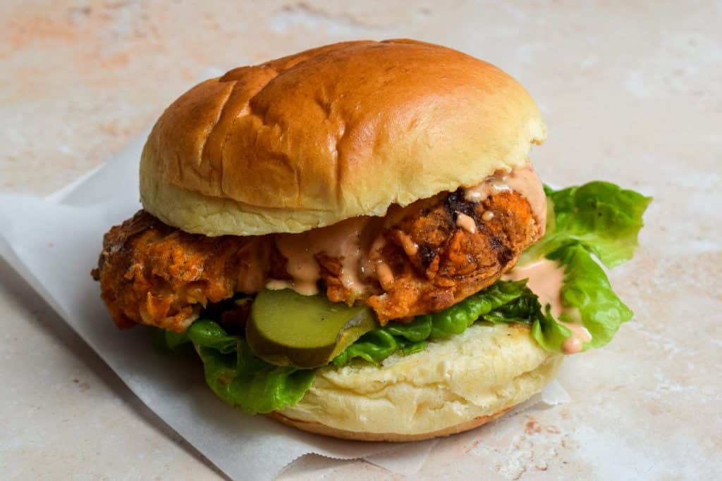 Fried chicken sandwich with lettuce, pickles, and sauce on a brioche bun.