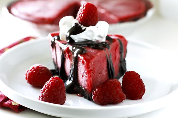 A slice of raspberry dessert topped with whipped cream, chocolate sauce, and fresh raspberries on a white plate.