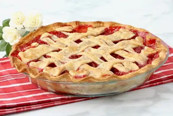 A freshly baked cherry pie with a lattice crust on a red striped cloth, next to white roses.