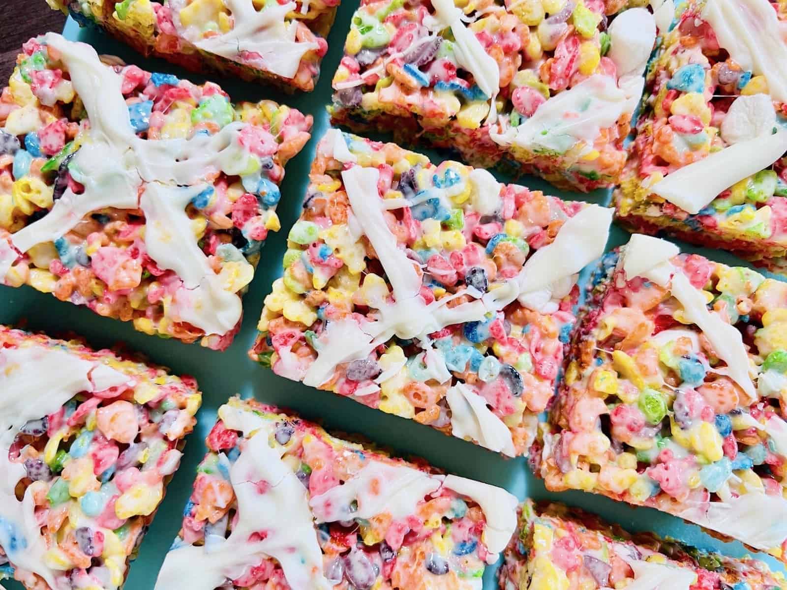 Colorful cereal bars with rainbow fruity pieces and white drizzle, cut into squares and arranged closely together.