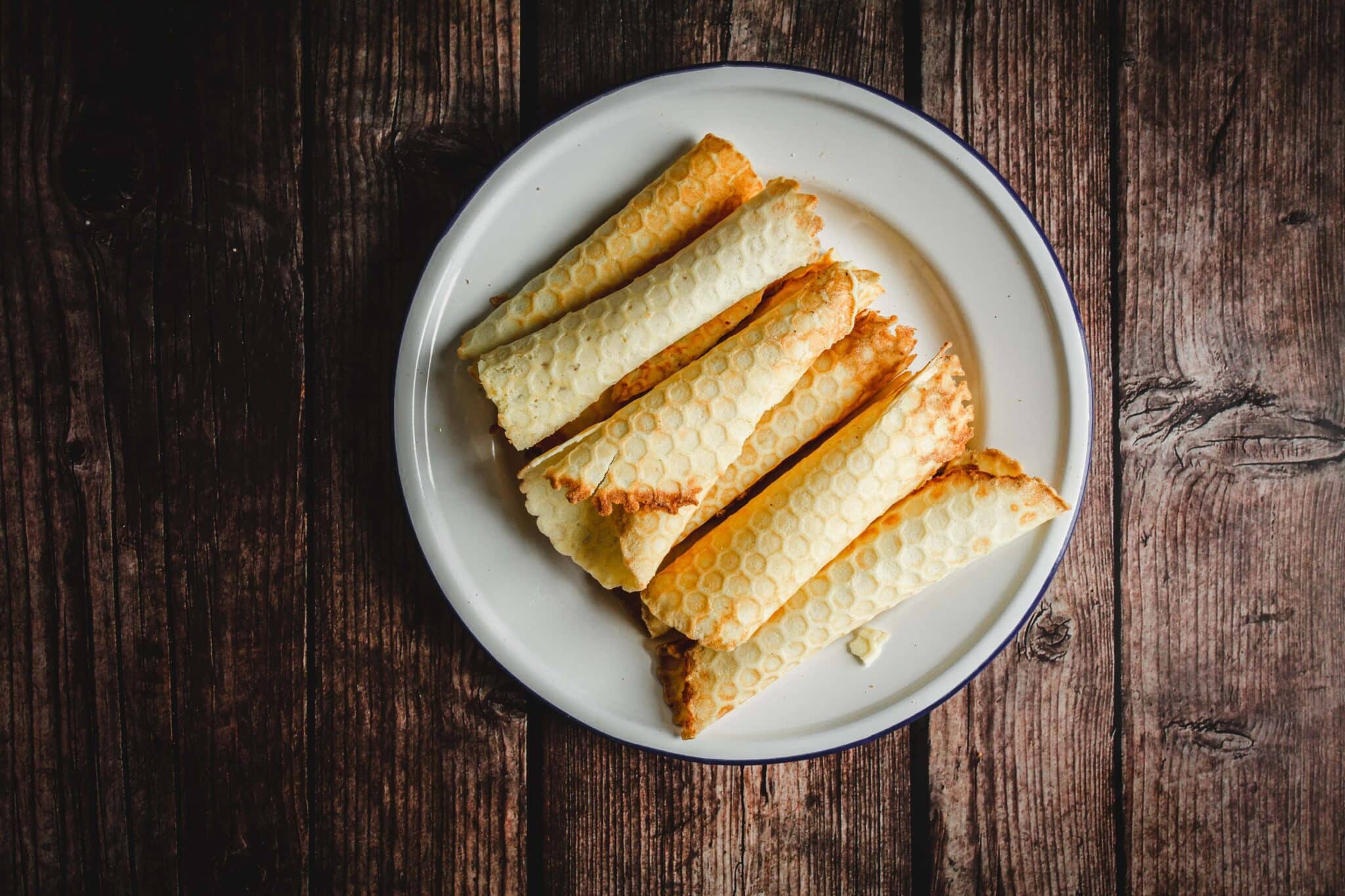 Six rolled honeycomb-patterned cookies on a white plate, set on a rustic wooden table.