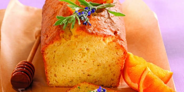 A loaf of orange bread garnished with herbs and flowers, served with honey dipper and orange slices.