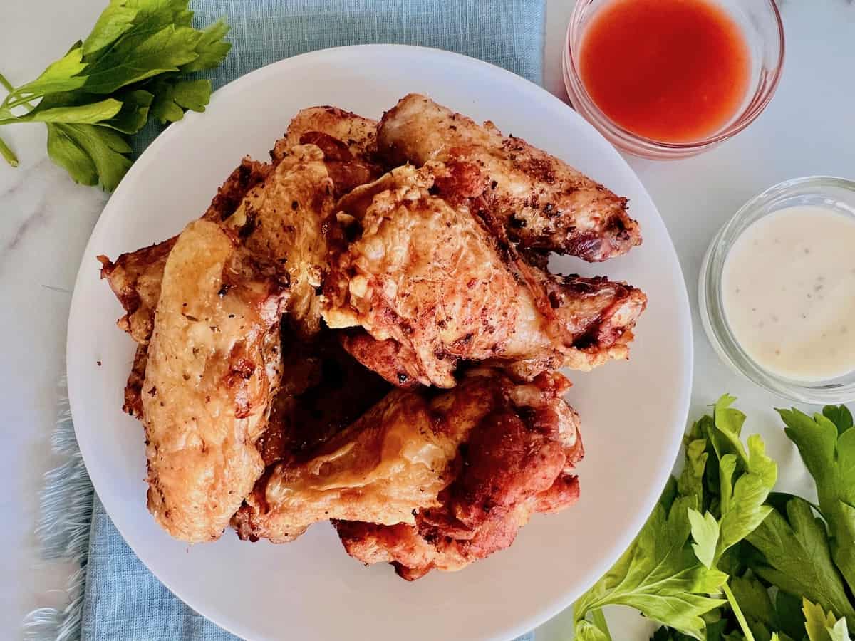 A plate of crispy fried chicken wings with cups of dipping sauces and fresh celery on the side.