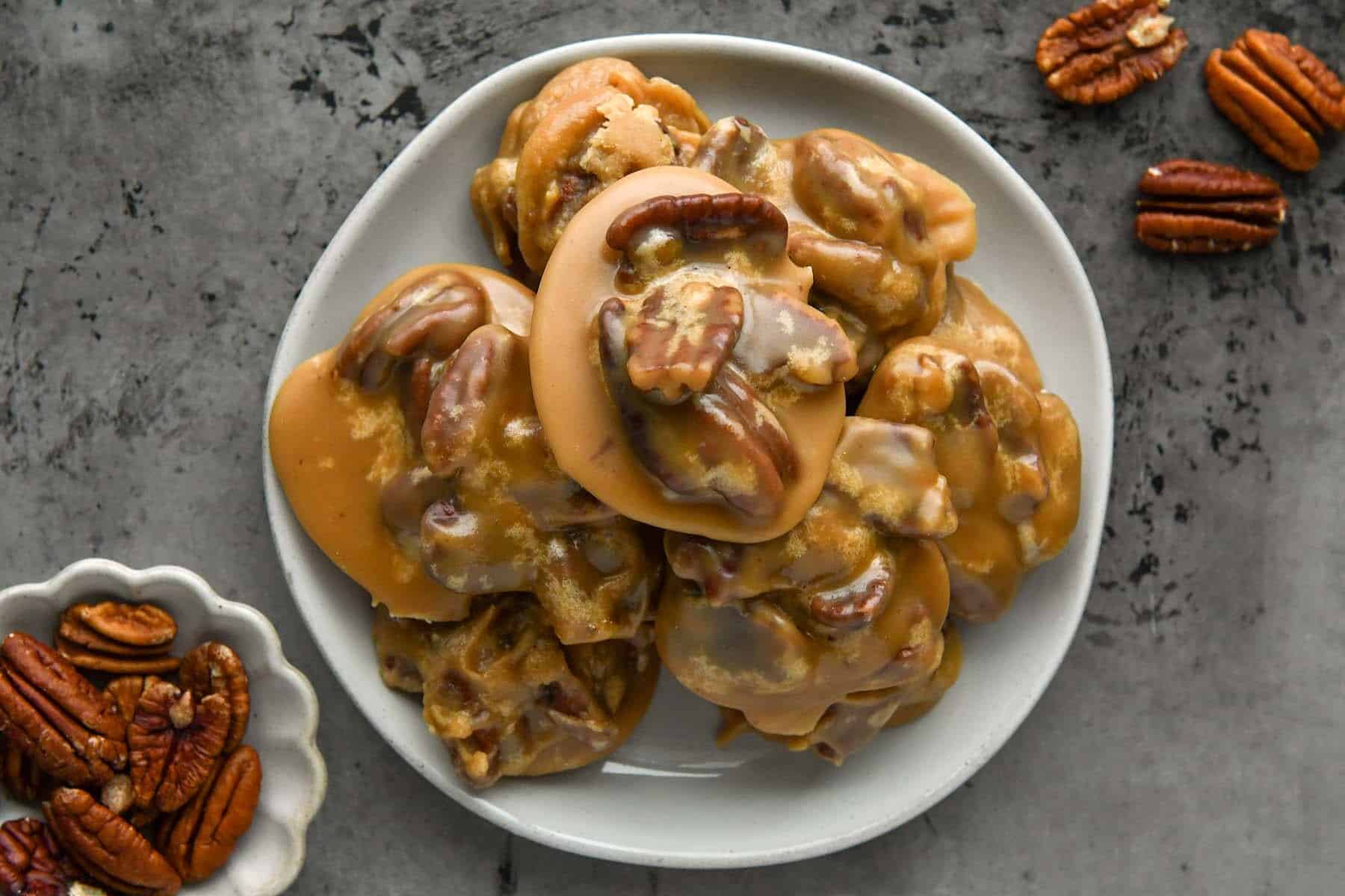A plate of pecan pralines covered in caramel glaze, with extra pecans on the side.