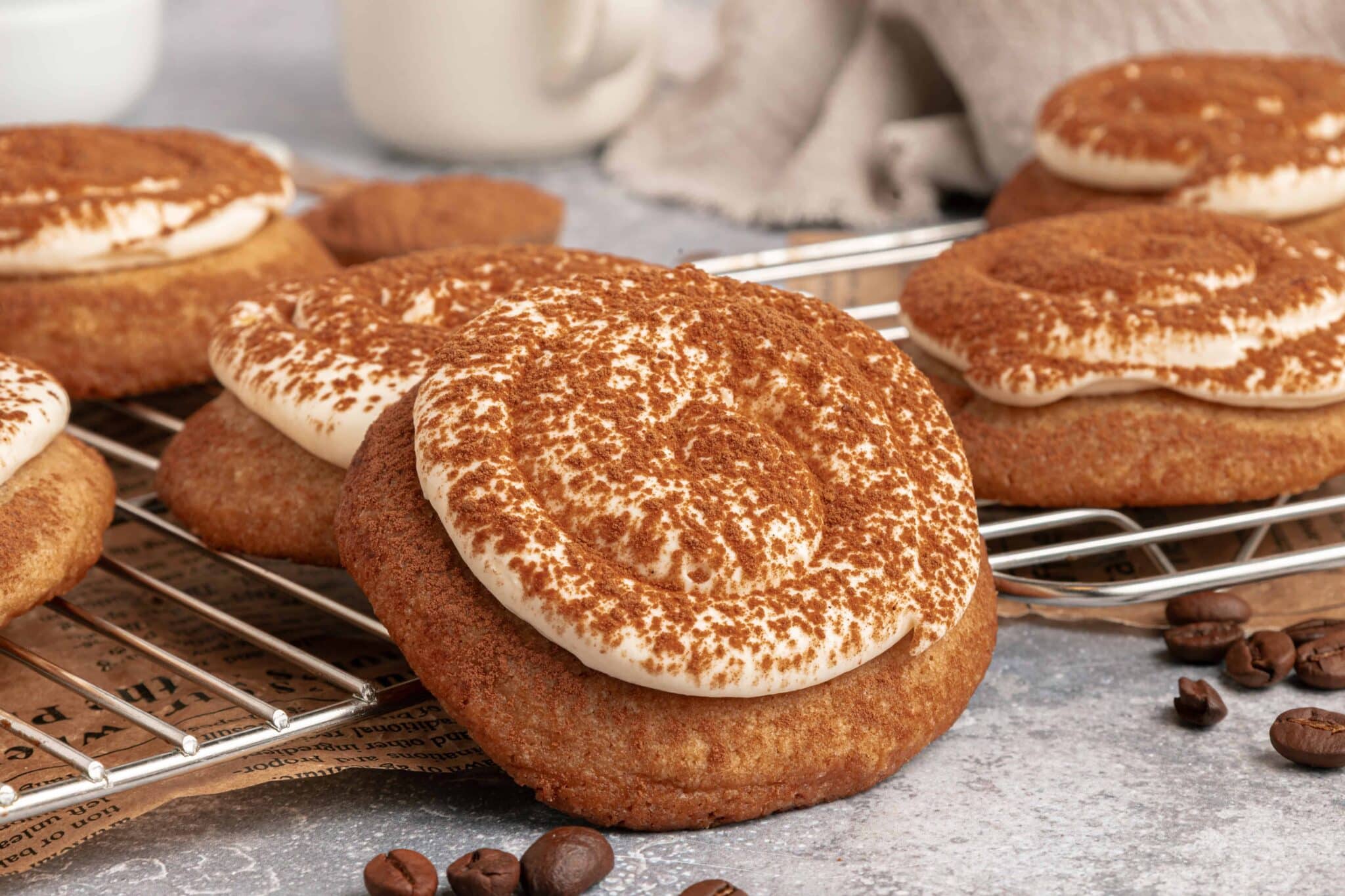 Large cookies with creamy frosting and cocoa powder, cooling on a wire rack with coffee beans nearby.