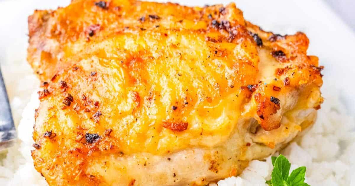 Golden-brown baked chicken breast served on a bed of white rice, garnished with a sprig of fresh parsley.