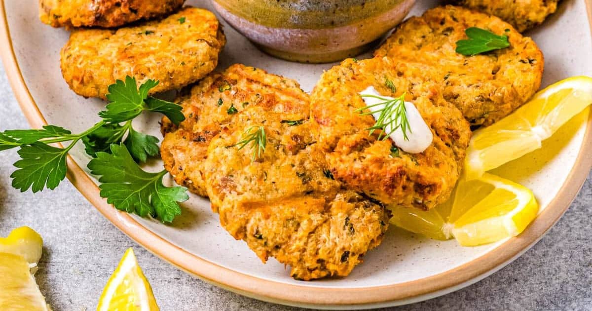 Plate of golden-brown salmon patties garnished with herbs, served with lemon wedges and parsley.
