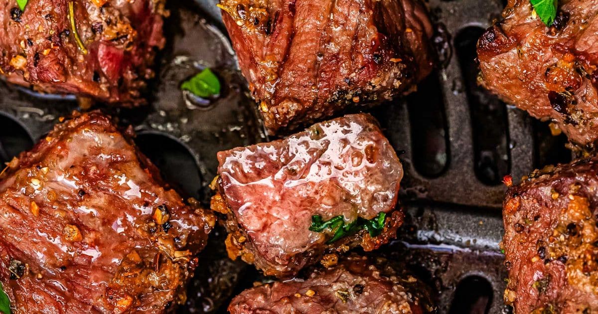 Close-up of juicy, seasoned steak bites cooked in an air fryer with visible herbs and spices.