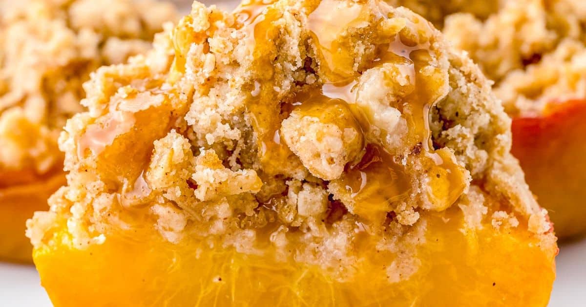 Close-up of a baked peach half topped with crumbly streusel and drizzled with honey or syrup.